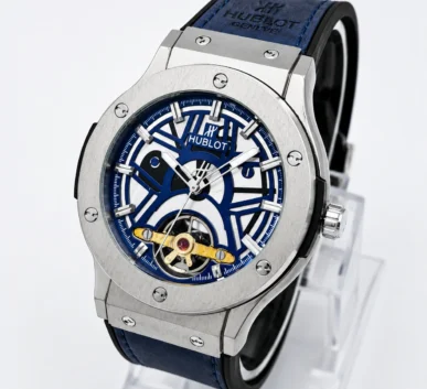 Blue skeleton dial luxury wristwatch with a silver stainless-steel case, blue strap, and visible gold mechanical movement.