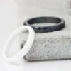 Black faceted ring and white ring displayed on a soft textured surface