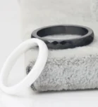 Black faceted ring and white ring displayed on a soft textured surface