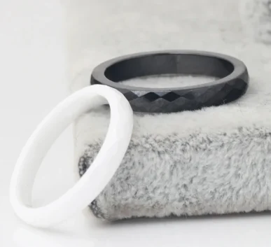 Black faceted ring and white ring displayed on a soft textured surface