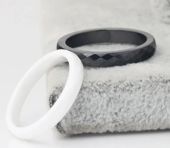 Black faceted ring and white ring displayed on a soft textured surface