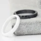 Black faceted ring and white ring displayed on a soft textured surface