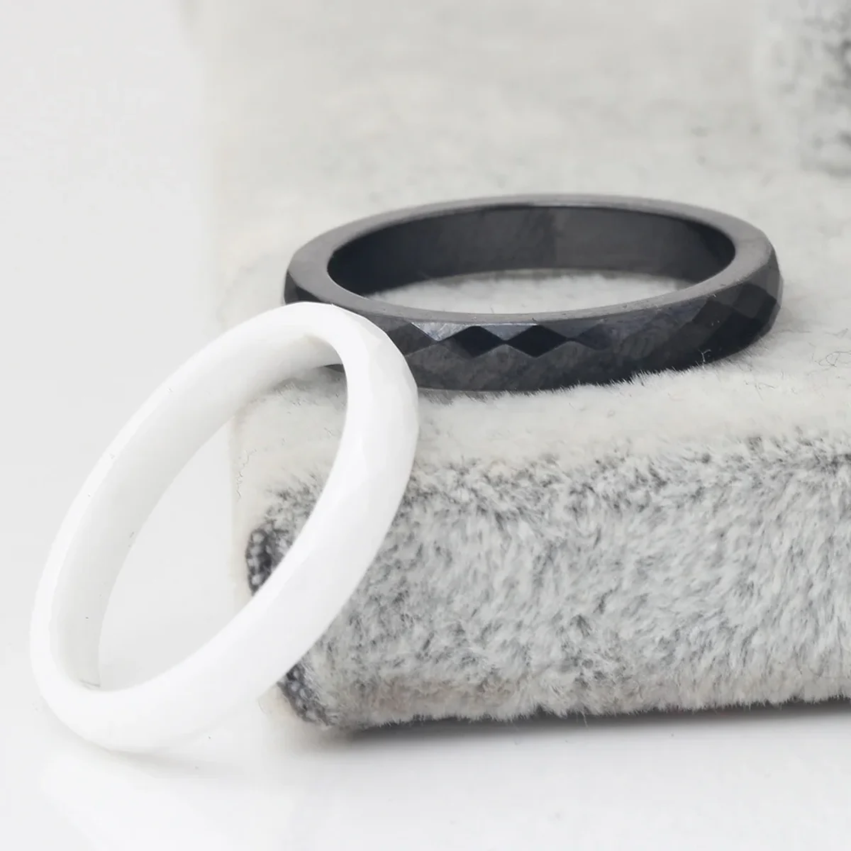 Black faceted ring and white ring displayed on a soft textured surface