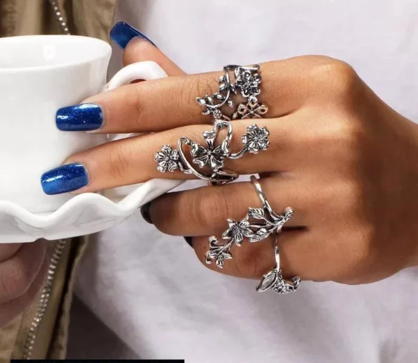 Ornate silver floral rings worn on a hand with blue nail polish