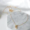Gold necklace with a delicate crescent moon pendant on a marble surface