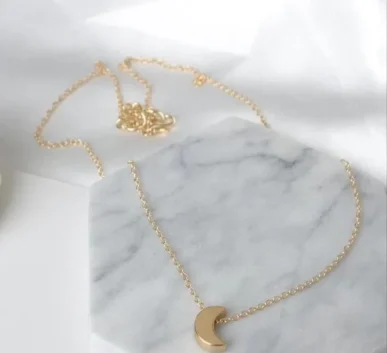 Gold necklace with a delicate crescent moon pendant on a marble surface