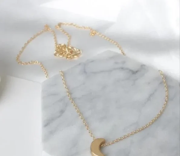 Gold necklace with a delicate crescent moon pendant on a marble surface