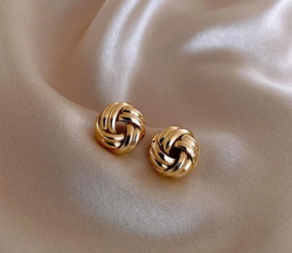 Elegant gold knot earrings on soft beige fabric