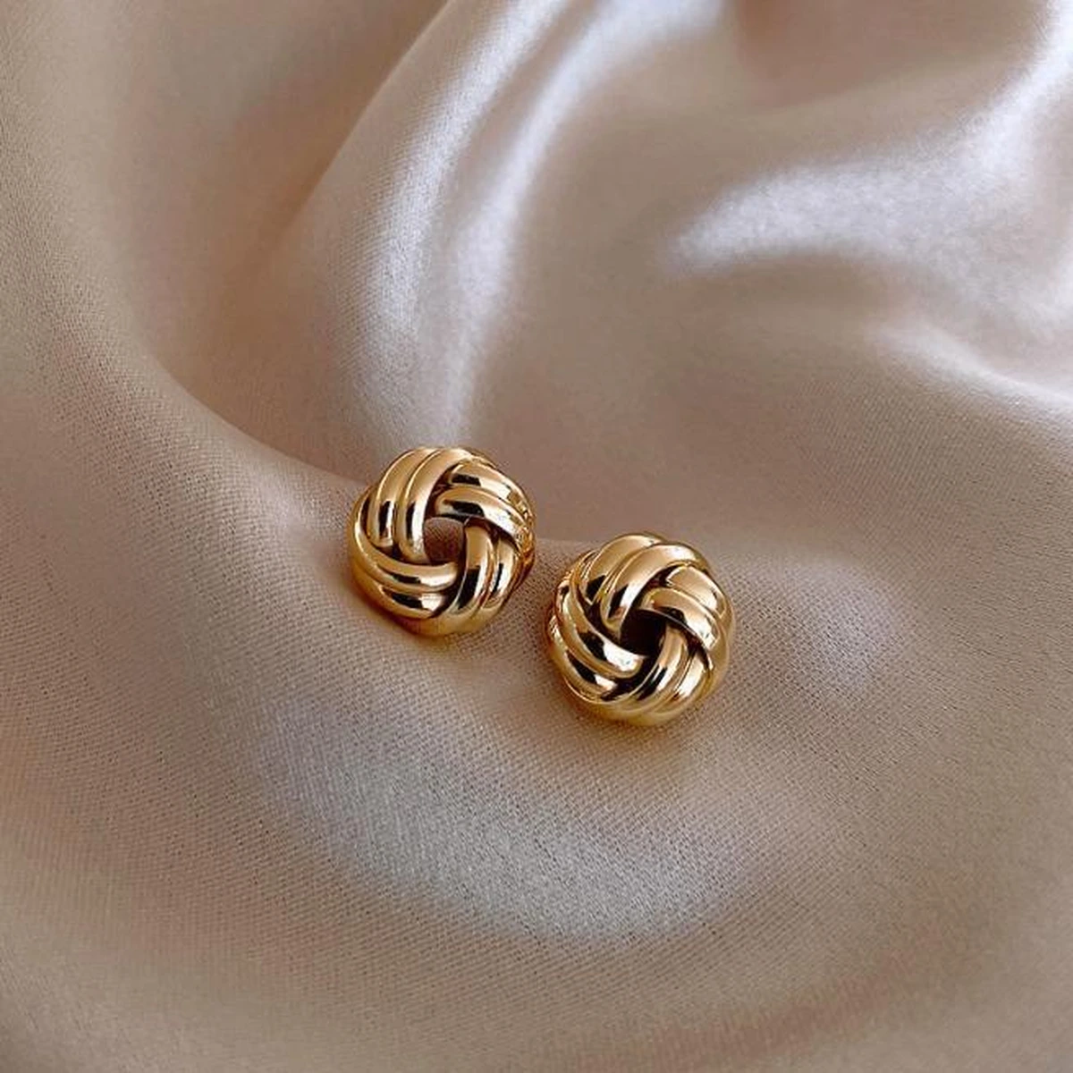Elegant gold knot earrings on soft beige fabric
