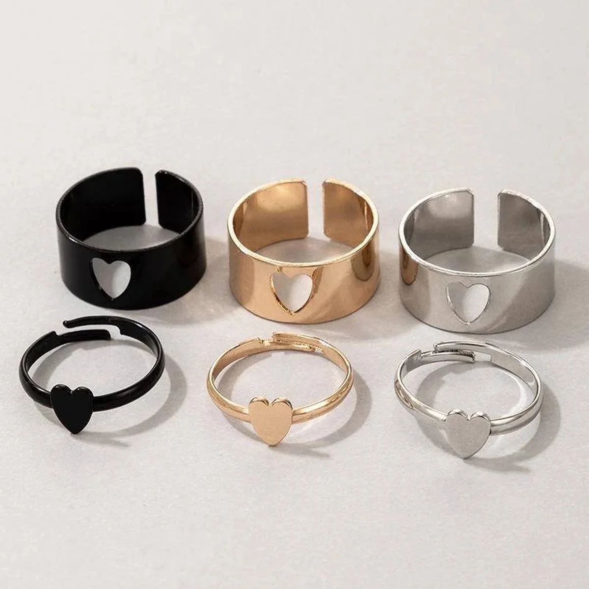 Collection of black, gold, and silver heart rings on a light background