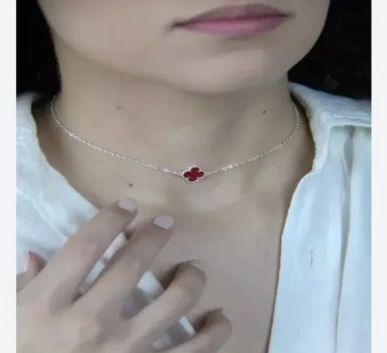 Delicate silver necklace with a red clover-shaped pendant worn around the neck