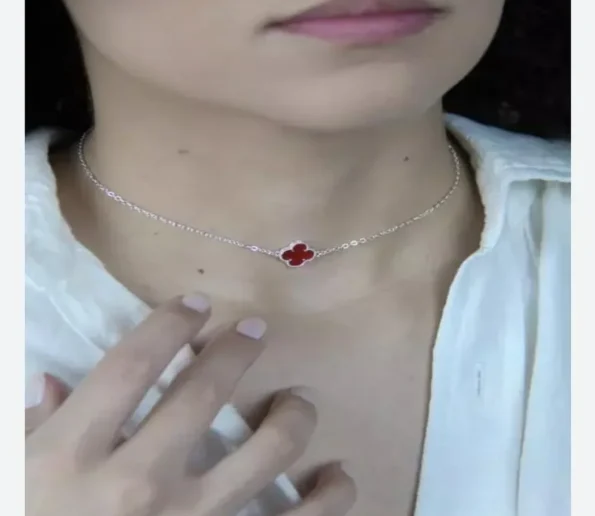 Delicate silver necklace with a red clover-shaped pendant worn around the neck