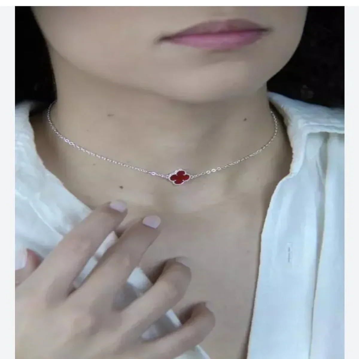 Delicate silver necklace with a red clover-shaped pendant worn around the neck
