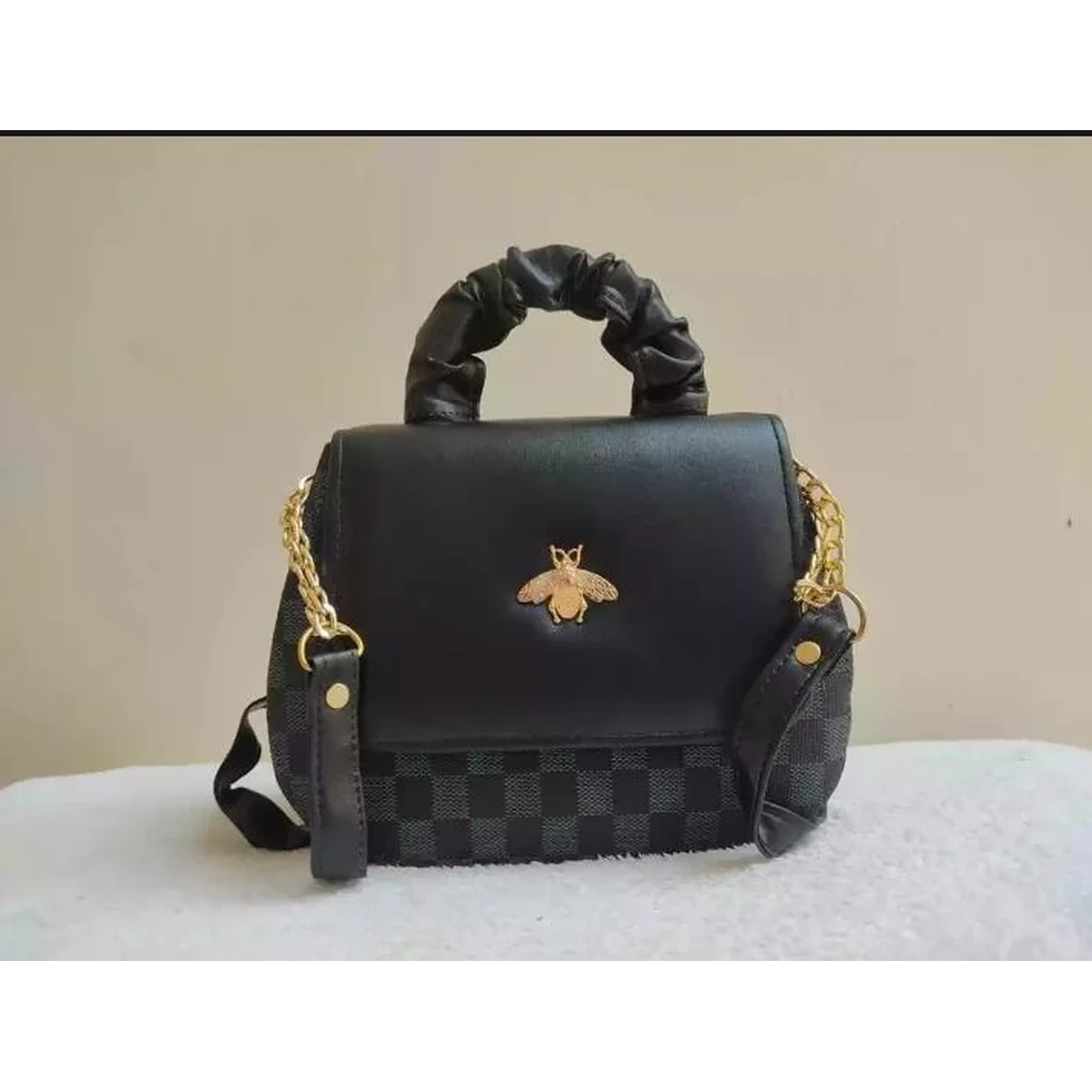 Black handbag with gold chain strap and bee-shaped decorative emblem
