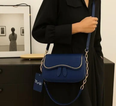 Elegant navy blue women’s shoulder bag with textured finish, curved flap, gold-tone trim, and chain strap.