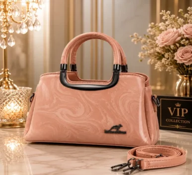 Elegant pink women’s handbag with dual handles, textured finish, and adjustable shoulder strap.