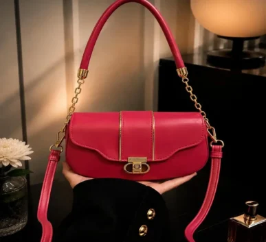 Red and pink women’s handbag with gold-tone hardware, top handle, long adjustable shoulder strap, and front clasp closure.