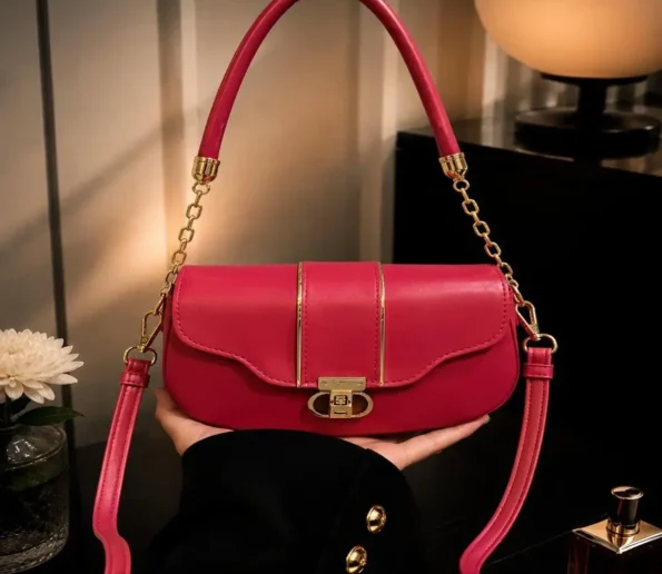 Red and pink women’s handbag with gold-tone hardware, top handle, long adjustable shoulder strap, and front clasp closure.
