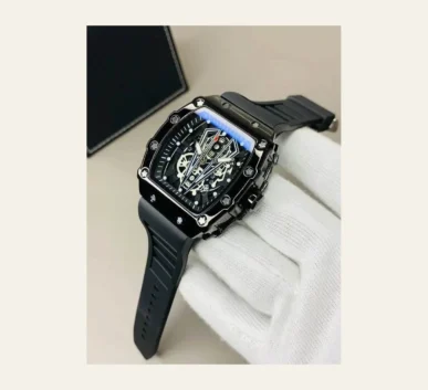 Black luxury skeleton watch with a detailed mechanical dial, rubber strap, and white glove against a beige background.